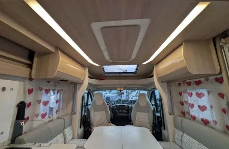 Intérieur d'un camping-car moderne avec sièges et table, rideaux à motifs de cœurs.