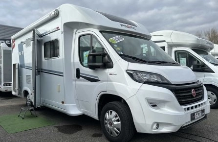 Camping-car blanc stationné sur un parking, modèle Pilote, ciel nuageux en arrière-plan.