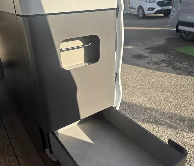Tiroir de rangement ouvert dans un camping-car, avec véhicules en arrière-plan