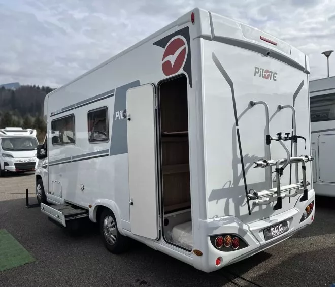 Camping-car Pilote stationné sur un parking avec porte ouverte et porte-vélos à l'arrière.