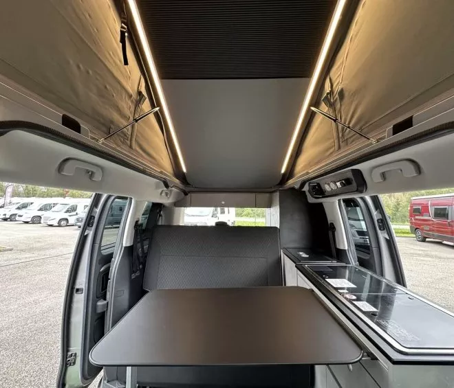 Intérieur d'un van aménagé avec table et banquette, éclairage LED