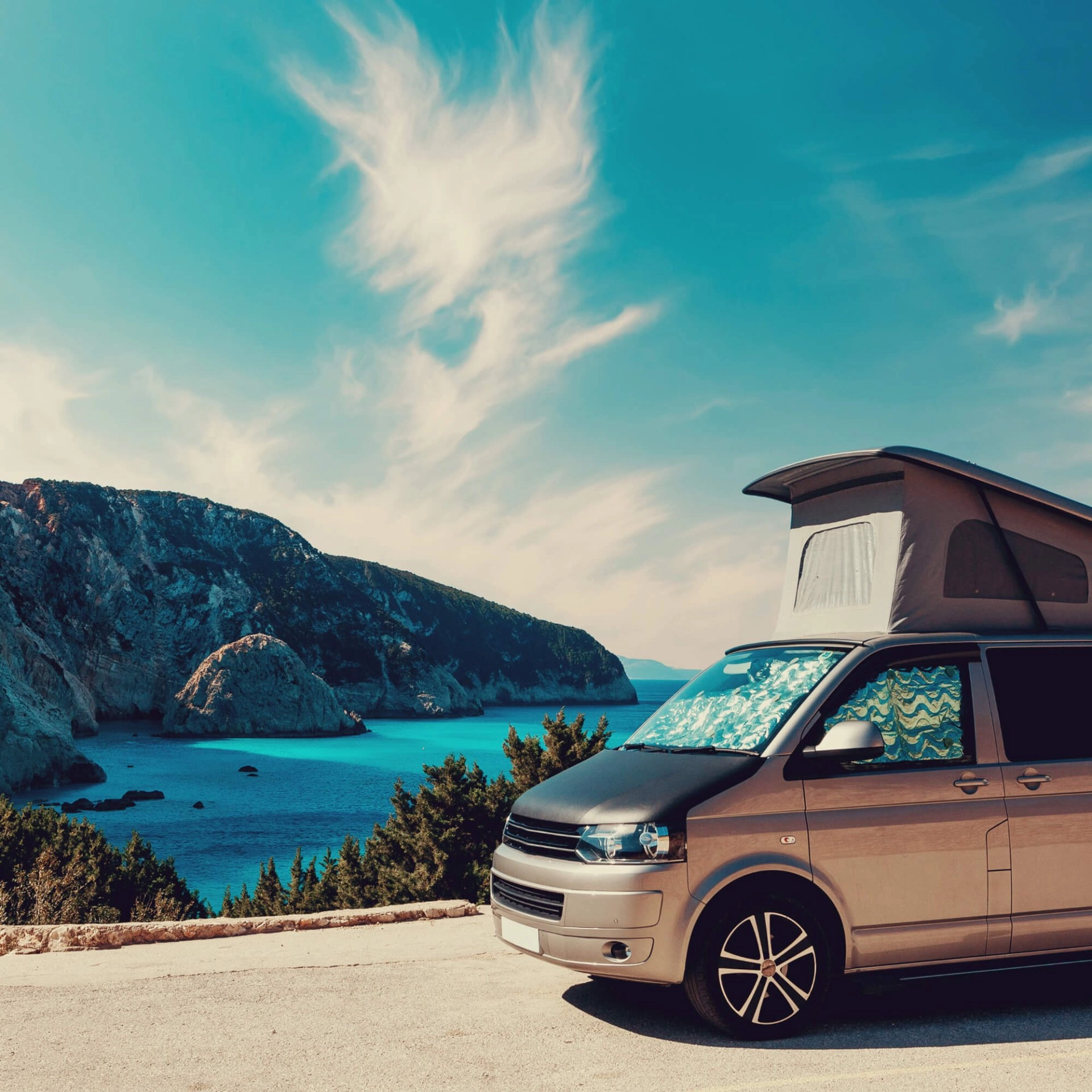 Van aménagé avec toit relevable face à une mer turquoise et falaises