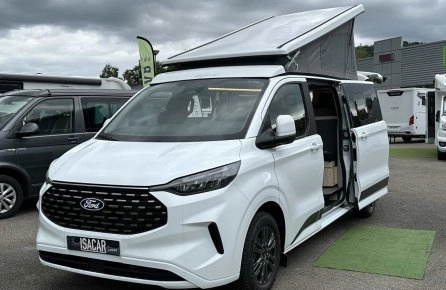 Van aménagé Ford blanc avec toit relevable sur un parking de concessionnaire.