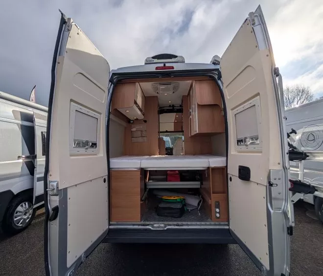 Intérieur d'un fourgon aménagé avec portes arrière ouvertes, ciel nuageux