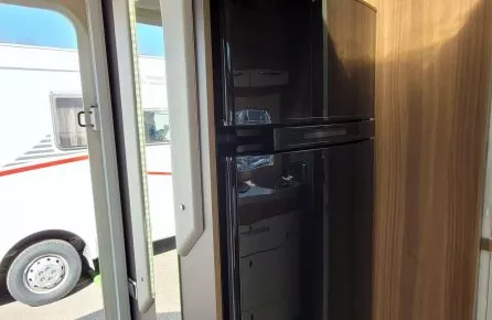 Intérieur d'un camping-car avec réfrigérateur intégré et porte ouverte sur l'extérieur.