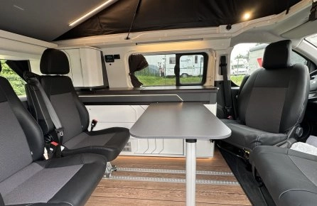 Intérieur d'un van aménagé avec sièges et table, sol en bois