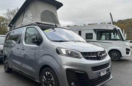Van Opel Crosscamp avec toit relevable sur un parking de camping-cars.