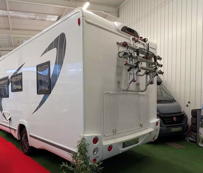 Camping-car blanc exposé dans un showroom avec porte-vélos à l'arrière.
