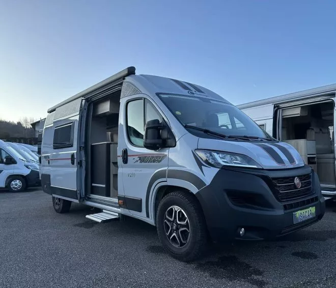 Camping-car gris stationné sur un parking, porte latérale ouverte