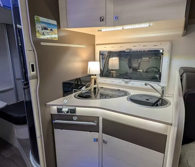 Cuisine compacte de camping-car avec évier, plaque de cuisson et éclairage intégré.