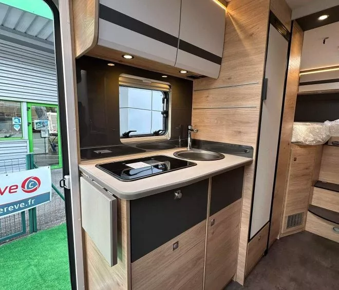 Cuisine moderne d'un camping-car avec évier, plaques de cuisson et rangements en bois clair.