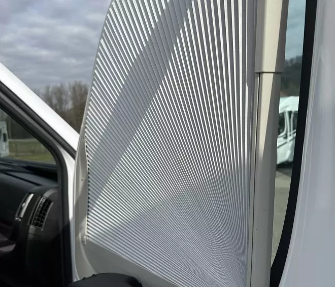 Store plissé blanc installé sur une fenêtre de véhicule utilitaire.