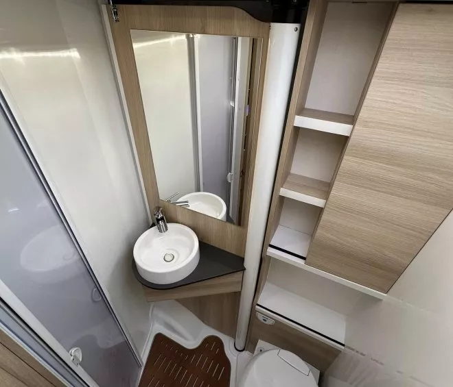 Salle de bain compacte avec lavabo, miroir et toilettes dans un camping-car moderne.
