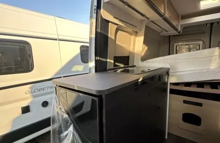Intérieur d'un camping-car moderne avec cuisine et lit, vue sur l'extérieur ensoleillé