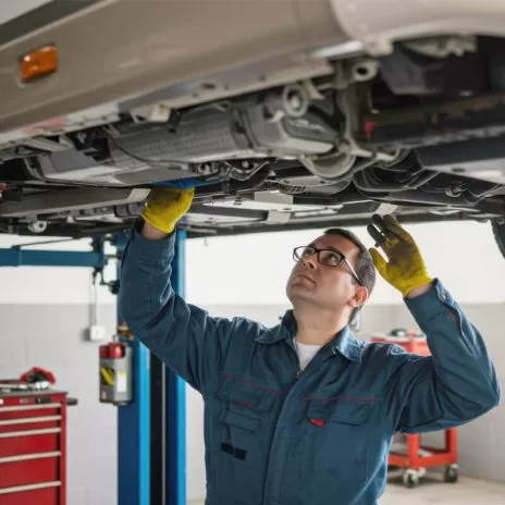 Mécanicien inspectant le dessous d'une voiture sur un pont élévateur dans un atelier.