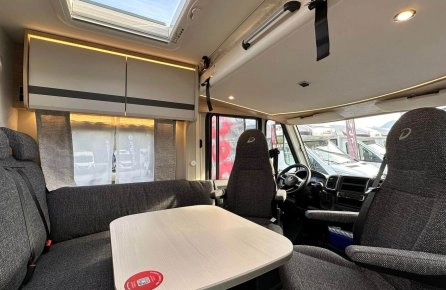 Intérieur d'un camping-car avec table, sièges et puits de lumière.