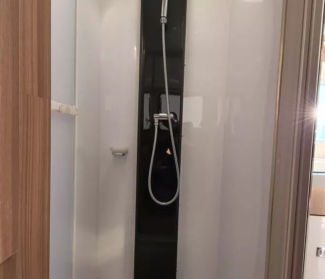 Douche moderne avec parois blanches et colonne noire dans un espace restreint.