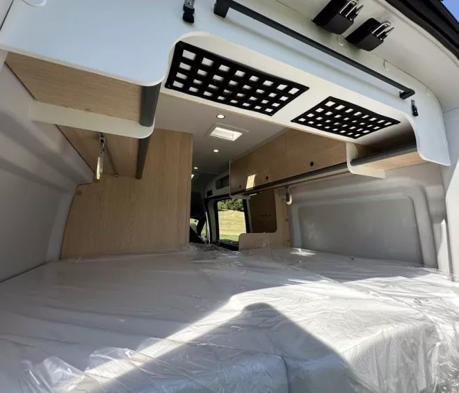 Intérieur d'un van aménagé avec lit et rangements en bois clair