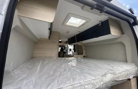 Intérieur d'un van aménagé avec lit et rangements en bois clair.