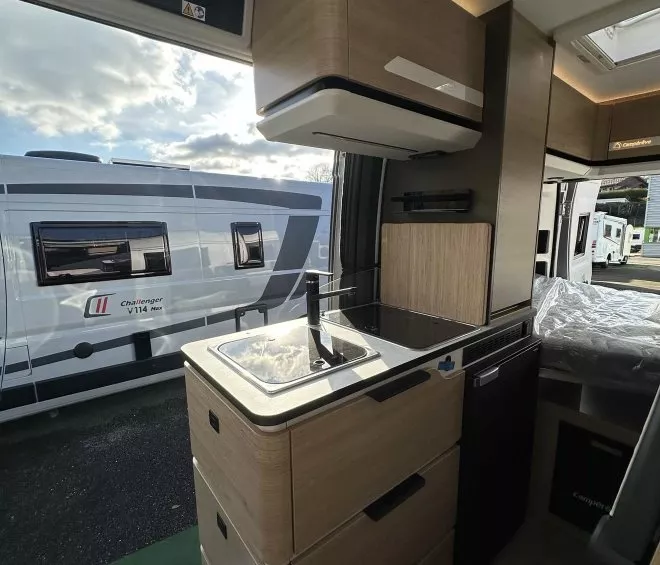Intérieur d'un camping-car moderne avec cuisine équipée et vue sur un autre véhicule stationné.