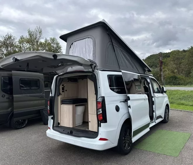 Van aménagé blanc avec toit relevable et portes ouvertes sur parking