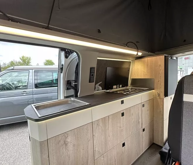 Intérieur d'un van aménagé avec cuisine moderne et espace de rangement en bois clair.