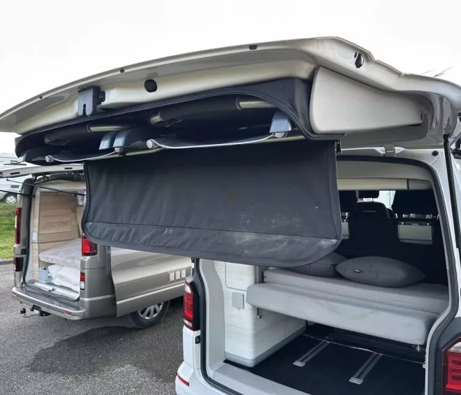 Vans aménagés avec lits rabattables et hayons ouverts sur un parking.
