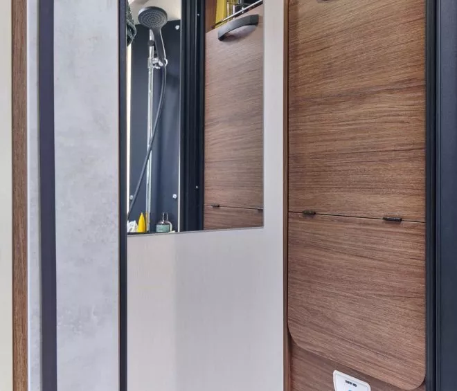 Salle de bain compacte avec douche et rangements en bois dans un camping-car moderne.