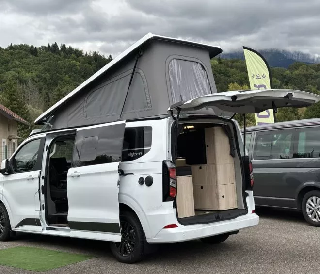 Van aménagé avec toit relevable et portes ouvertes, stationné en extérieur