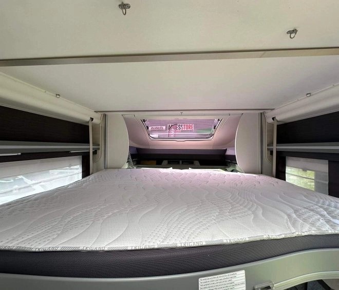 Intérieur d'un camping-car avec un lit double et un hublot ouvert
