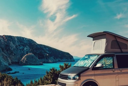 Van aménagé avec toit relevable face à une mer turquoise et falaises