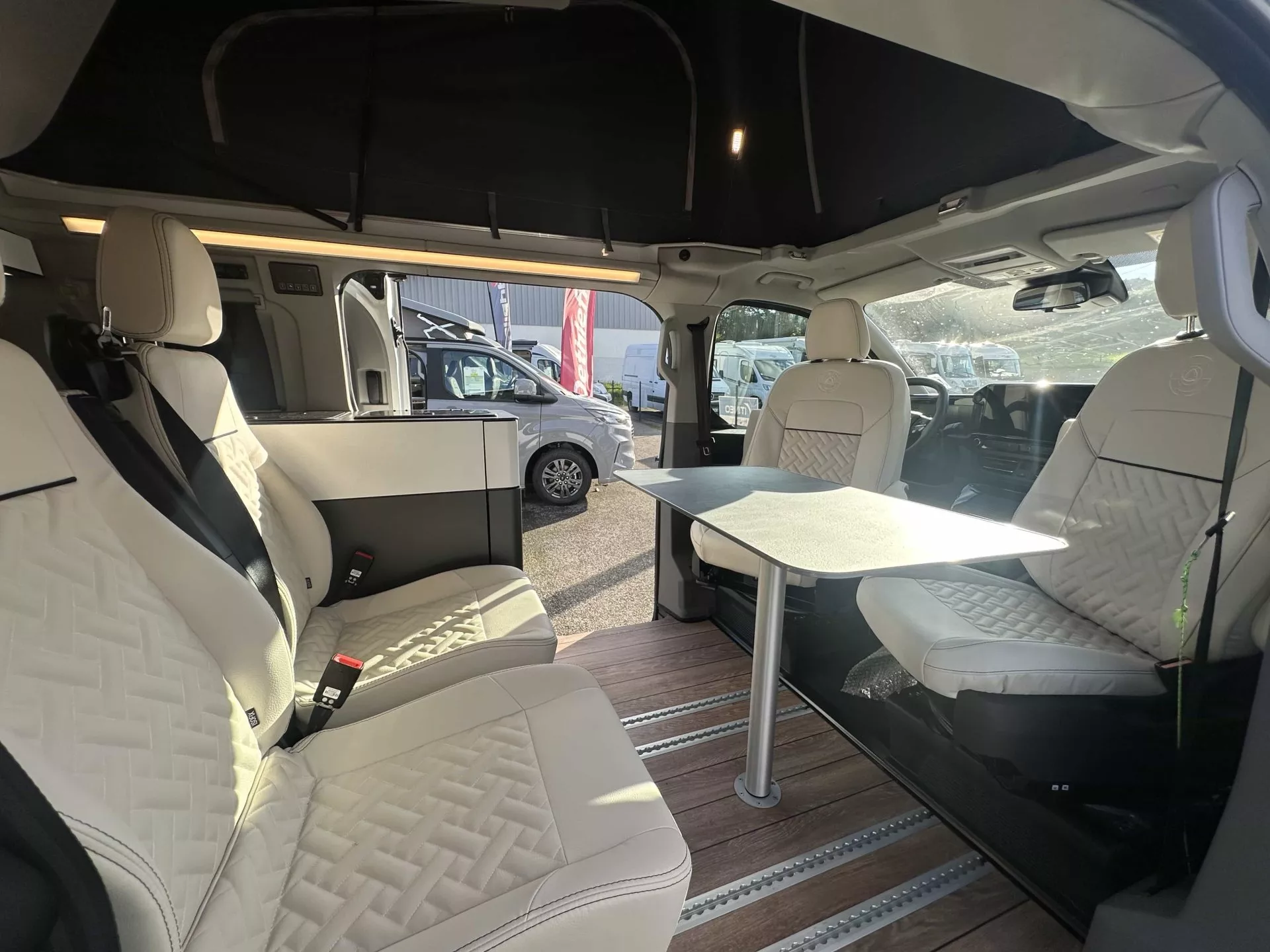 Intérieur d'un van aménagé avec sièges en cuir et table pliante, idéal pour le camping.