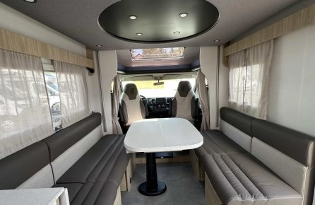 Intérieur spacieux d'un camping-car moderne avec banquettes et table centrale.