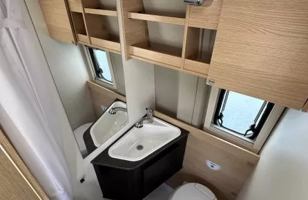 Salle de bain compacte avec lavabo, toilettes et rangements en bois clair dans un camping-car.