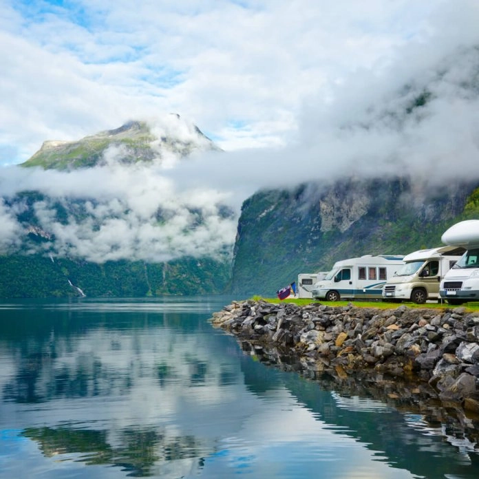 Camping-cars stationnés au bord d'un fjord norvégien avec montagnes et nuages en arrière-plan