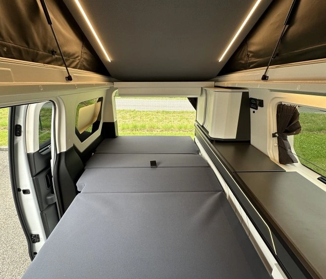 Intérieur d'un van aménagé avec lit replié et éclairage LED