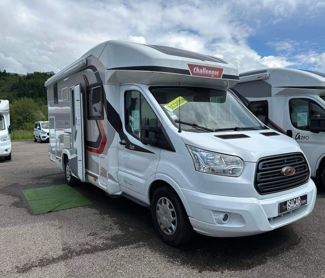 Camping-car Challenger blanc stationné sur un parking, ciel nuageux en arrière-plan.