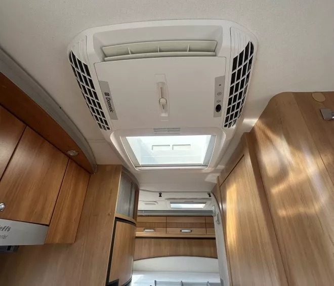 Intérieur d'un camping-car avec placards en bois et système de ventilation au plafond.