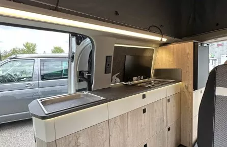 Intérieur d'un van aménagé avec cuisine moderne et espace de rangement en bois clair.