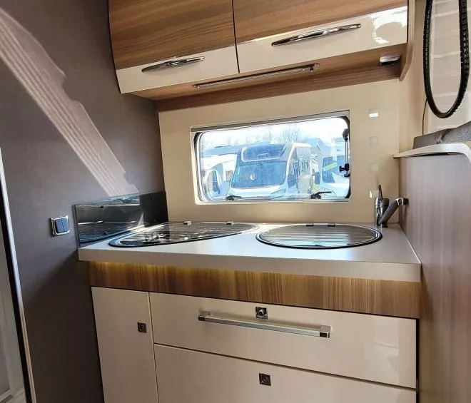 Cuisine compacte de camping-car avec placards en bois et fenêtre.