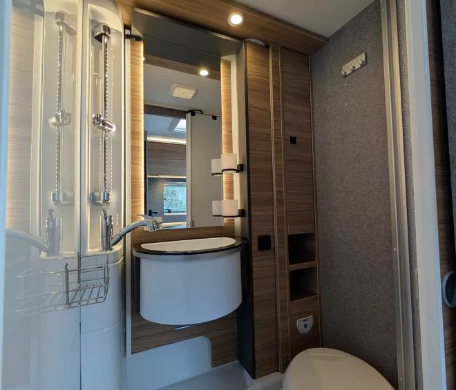 Salle de bain moderne dans un camping-car avec douche, lavabo et toilettes.