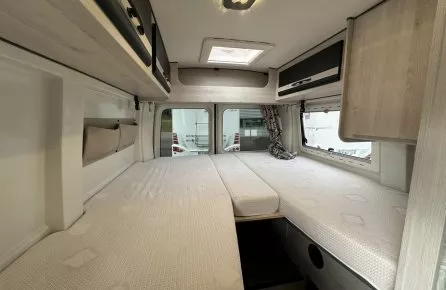 Intérieur d'un camping-car avec lits jumeaux et rangements en bois clair.