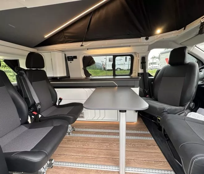 Intérieur d'un van aménagé avec sièges et table, sol en bois