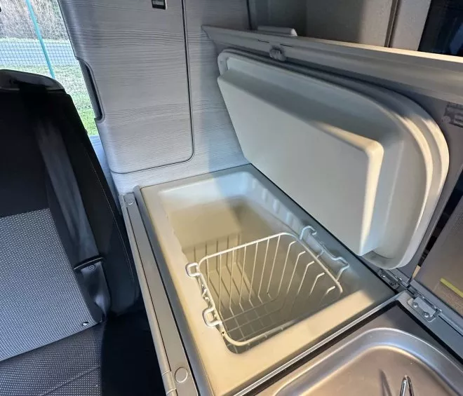 Intérieur d'un van aménagé avec réfrigérateur ouvert et évier intégré.