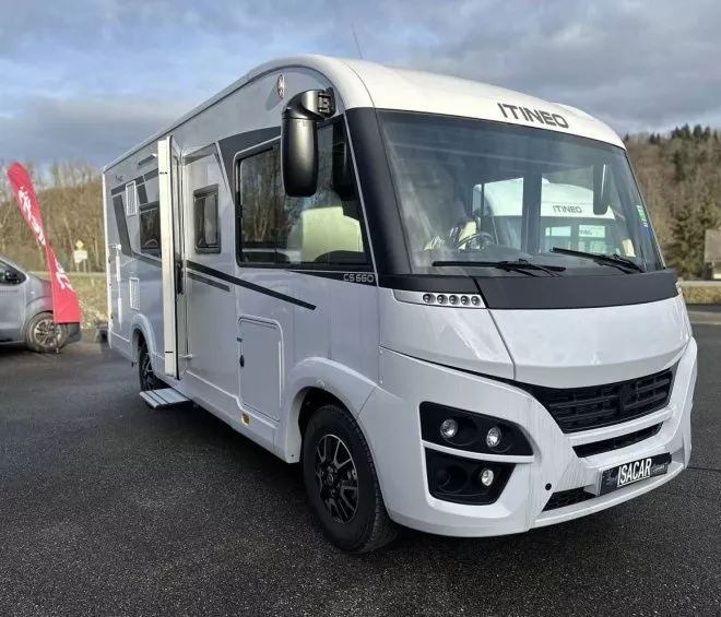 Camping-car Itineo blanc stationné sur un parking, ciel nuageux en arrière-plan.