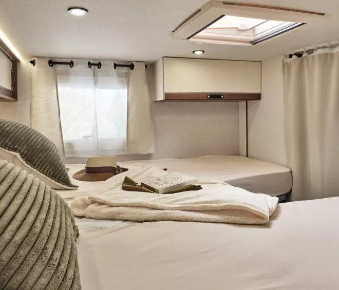 Intérieur d'un camping-car avec lit, coussins et lumière naturelle.