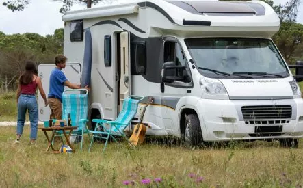Camping-car stationné dans un champ avec deux personnes et des chaises pliantes.