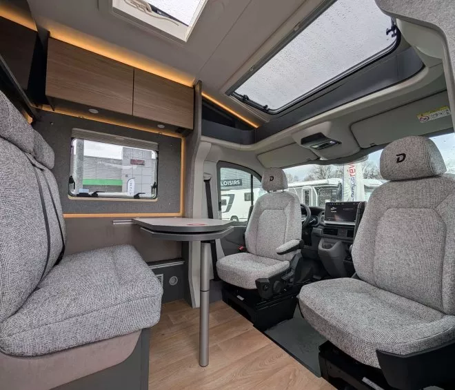 Intérieur d'un camping-car moderne avec sièges en tissu gris et table pliante.