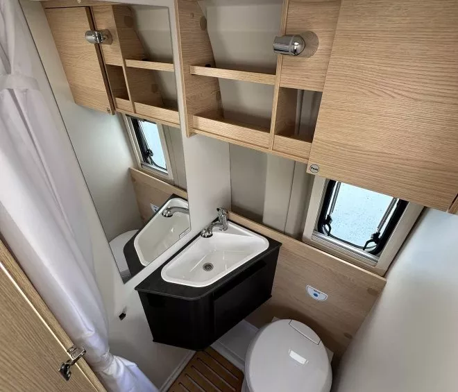 Salle de bain compacte avec lavabo, toilettes et rangements en bois clair dans un camping-car.