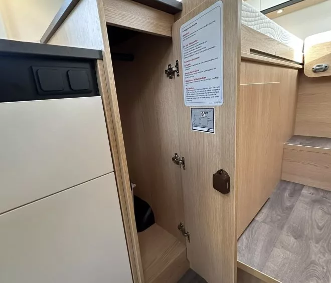 Intérieur d'un camping-car avec placard en bois ouvert et lit surélevé.